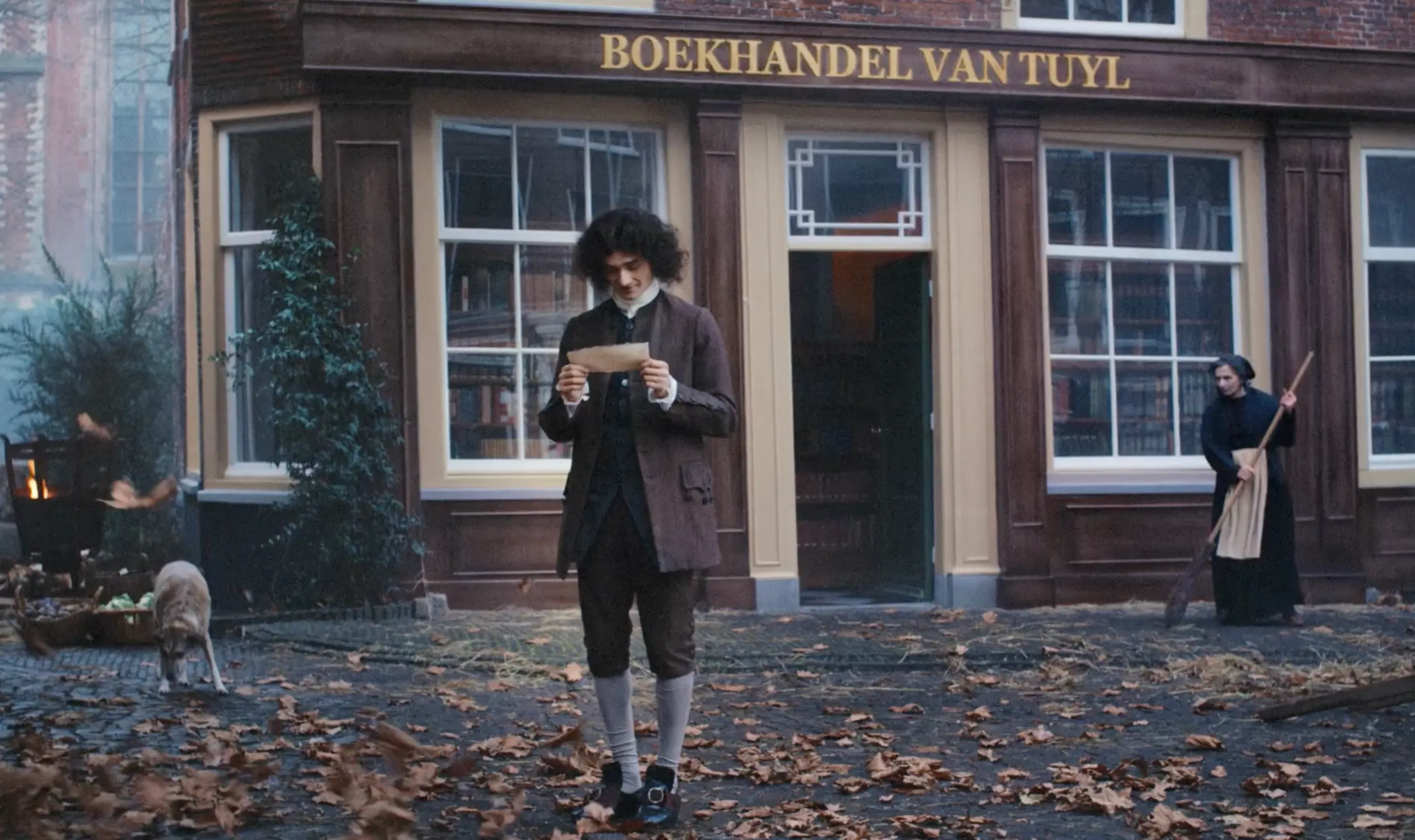 Man staat voor Boekhandel van Tuyl met een briefje in zijn handen, bladeren liggen op de grond.