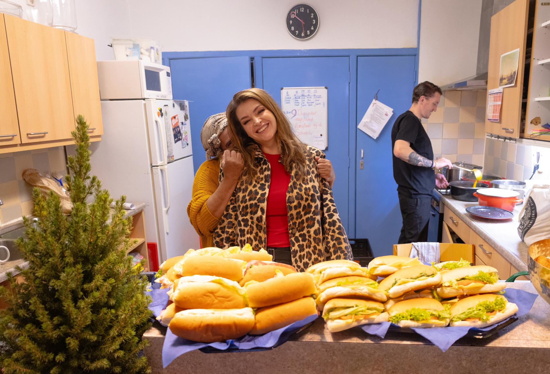 Twee vrouwen in een keuken met een groene kerstboom en een tafel vol hotdogs.
