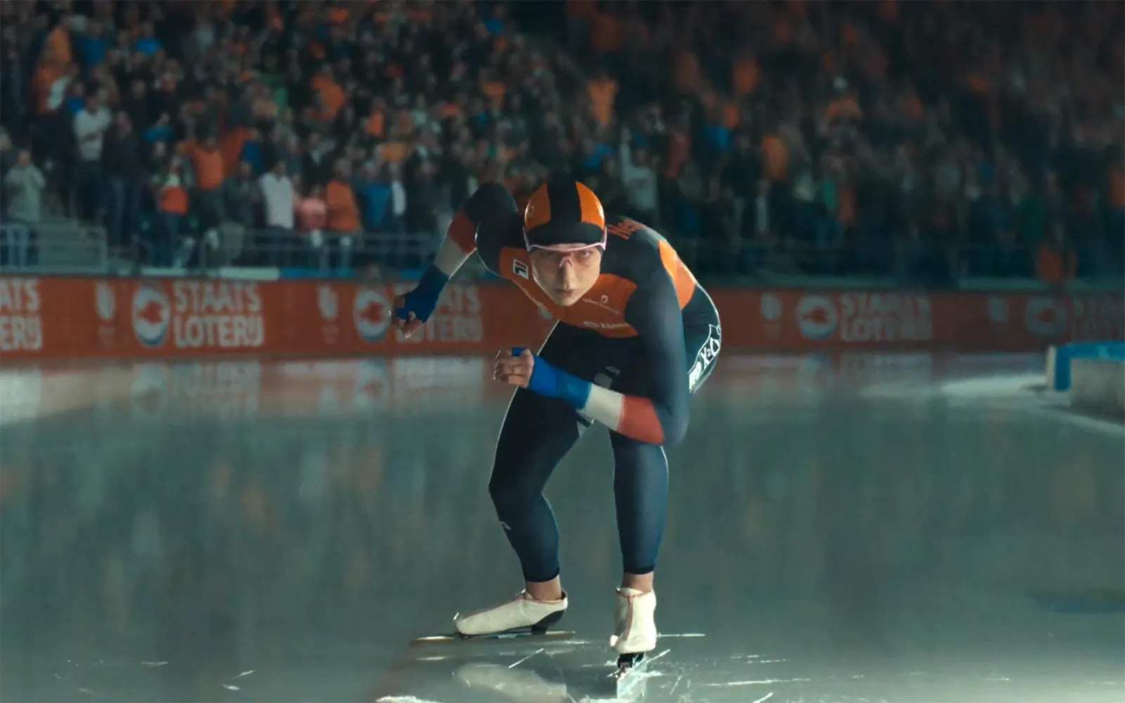 Schaatser in actie op het ijs met enthousiaste toeschouwers op de achtergrond.