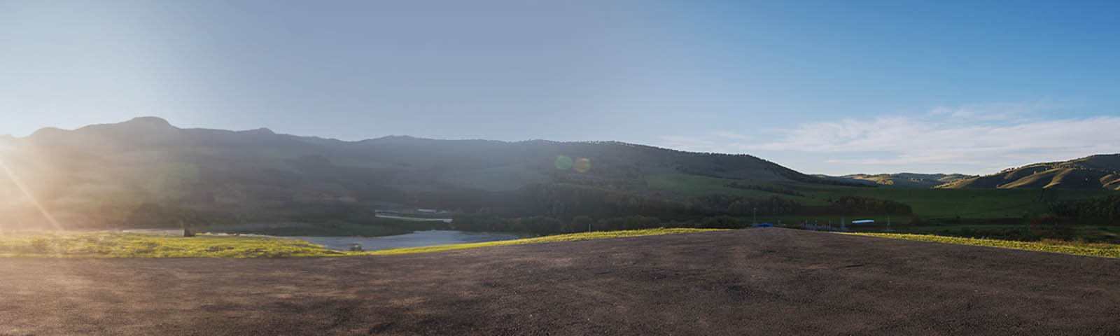 Uitzicht op groene heuvels en heldere lucht met de zon die opkomt.