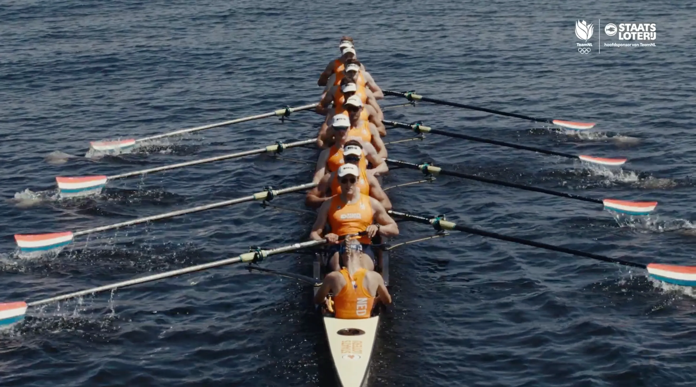 Een ploeg van roeiers in oranje kleding in een boot op het water.