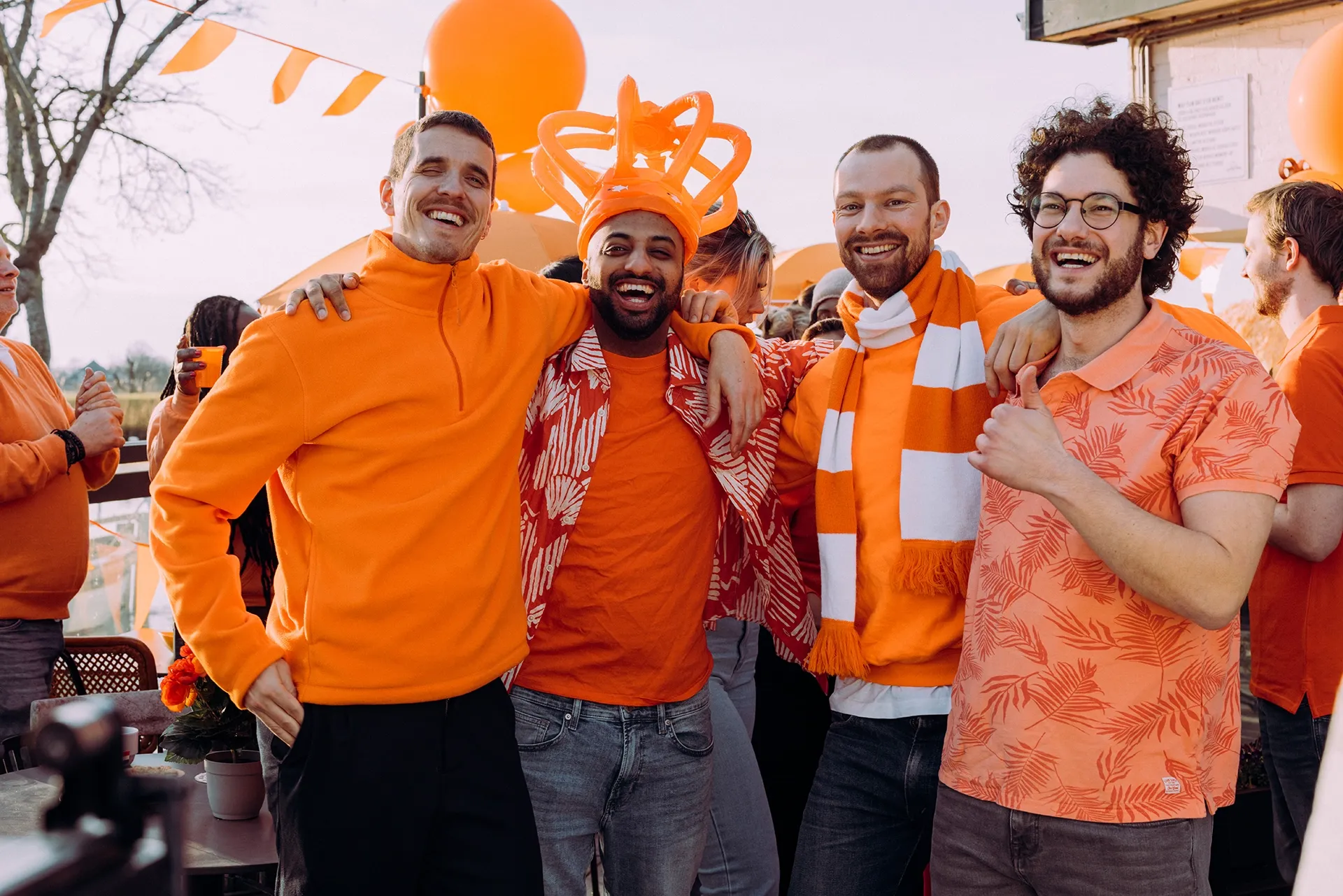 Groep mensen in oranje kleding tijdens een feestelijke gelegenheid, omgeven door oranje decoraties.
