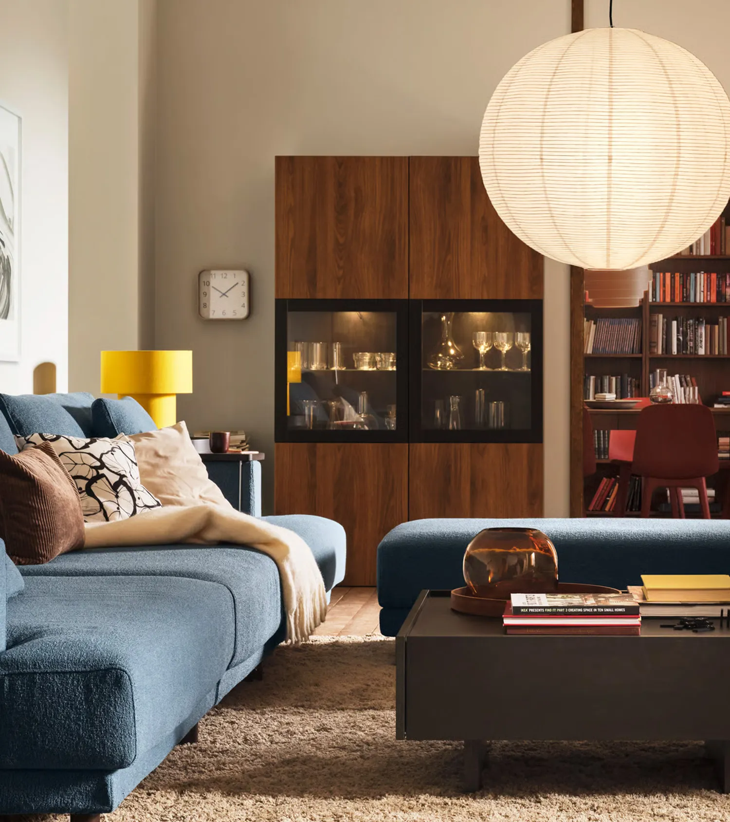 Moderne woonkamer met blauwe bank, houten kast en grote lamp.