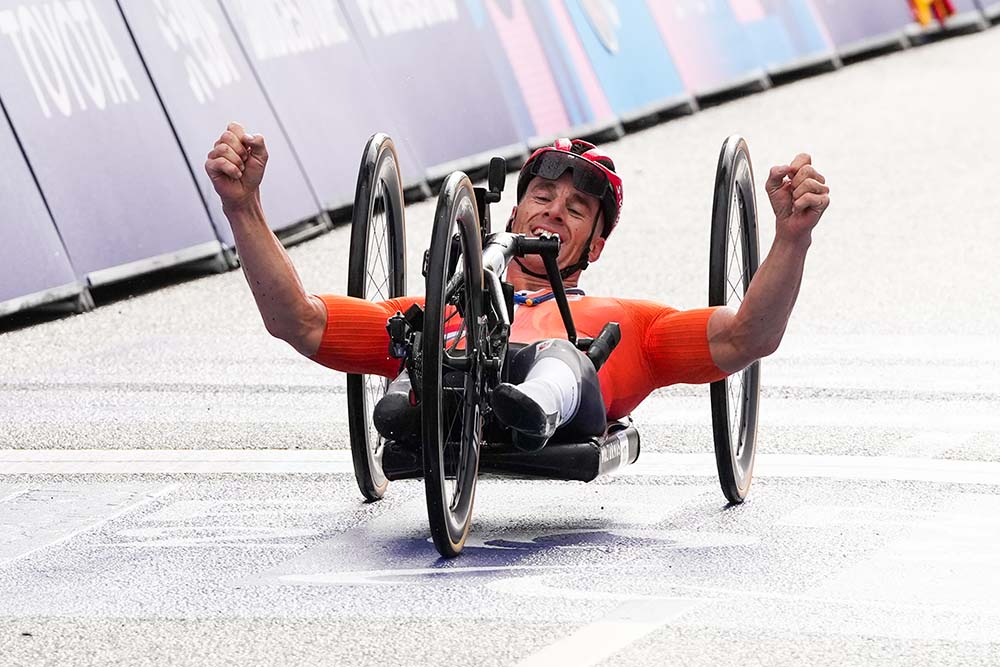 Atleet in een handbike juicht na het behalen van de finishlijn