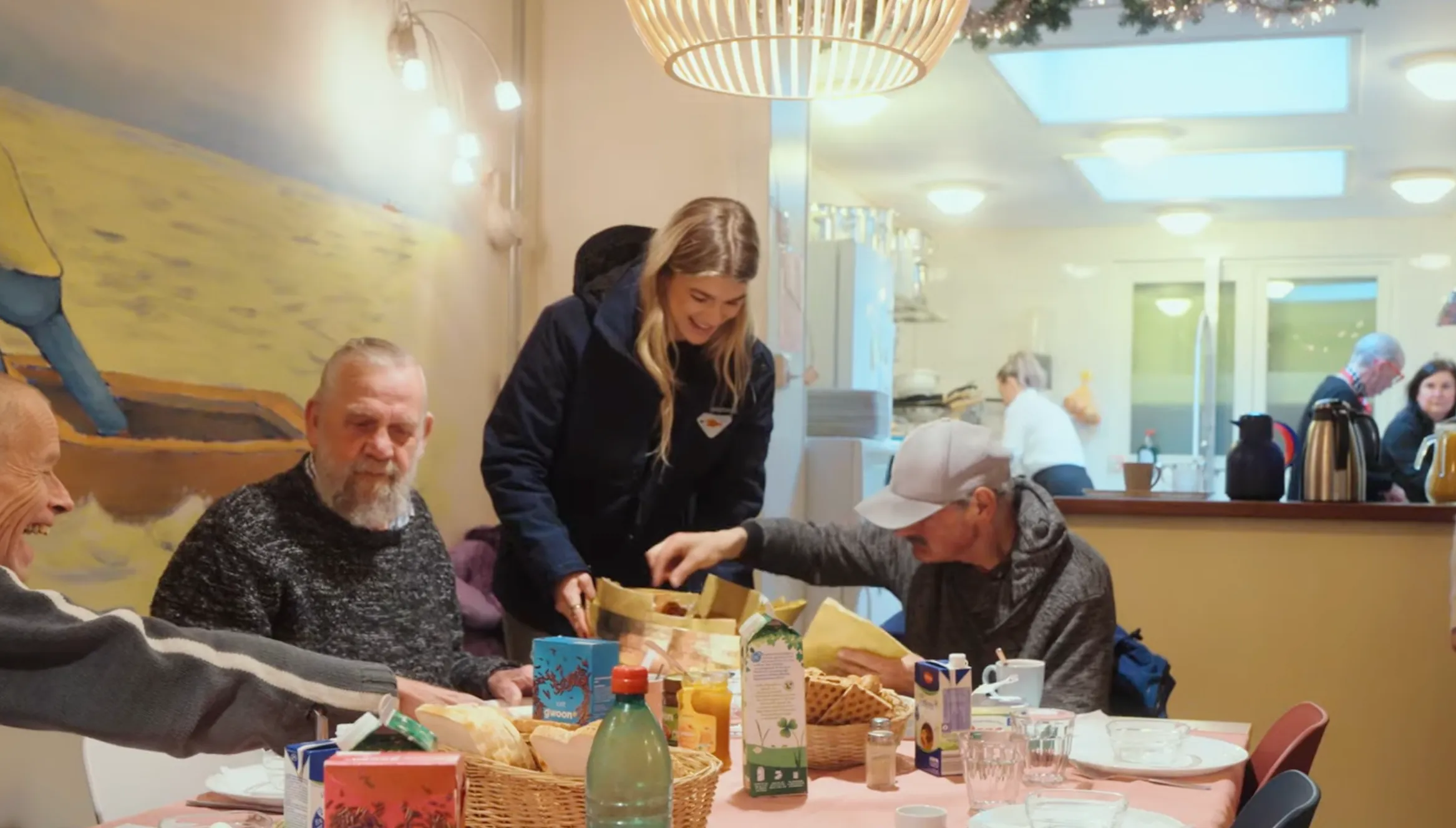 Een vrouw serveert voedsel aan een tafel met mensen, in een gezellige eetomgeving.
