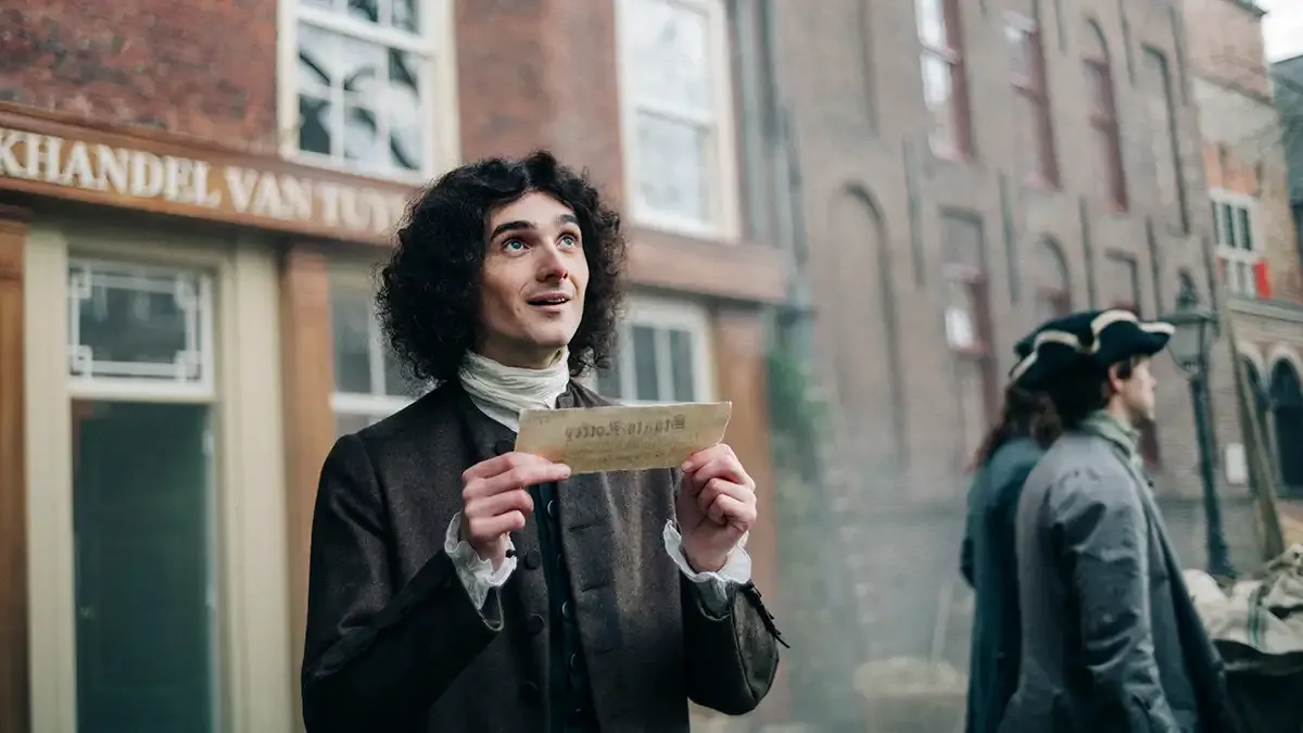 Een man in historische kledij houdt een oud stuk papier vast, op de achtergrond zijn andere mensen in vergelijkbare kleding.