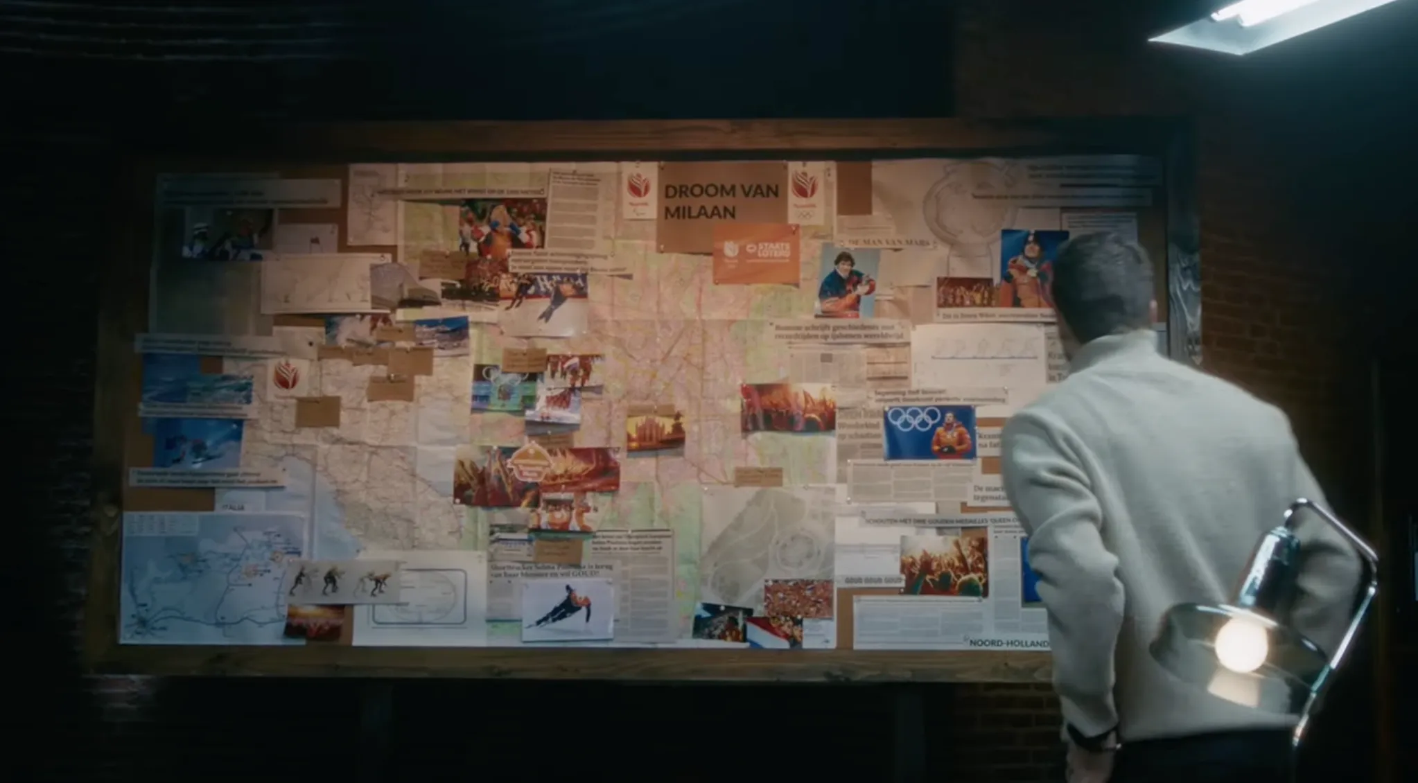 Een persoon bekijkt een informatiebord met krantenknipsels en kaarten over de Droom van Milaan.