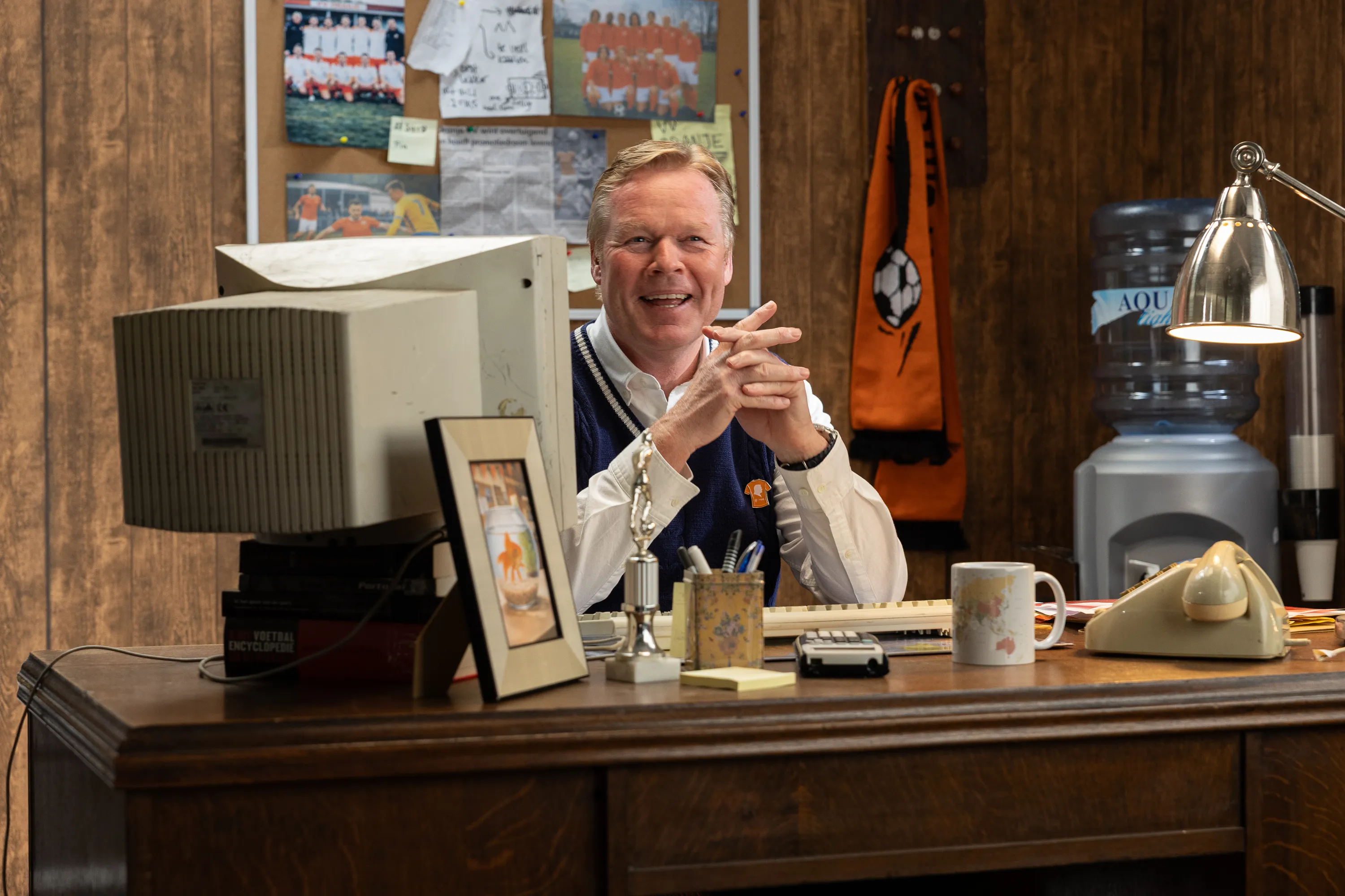 Een bureautafel met een computer, kantoorbenodigdheden en een achtergrond met sportposters.