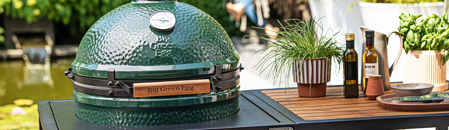 Big Green Egg op een tafel met kruiden en oliën eromheen