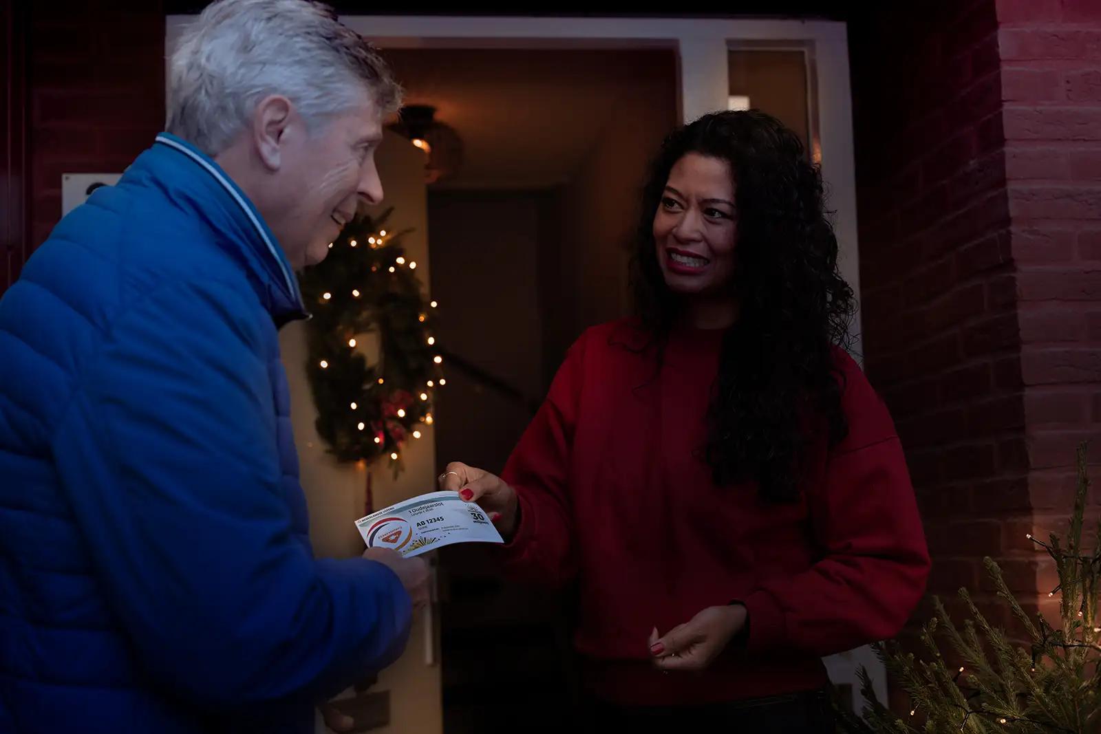 Een vrouw geeft een Staatslot aan een man aan de voordeur.